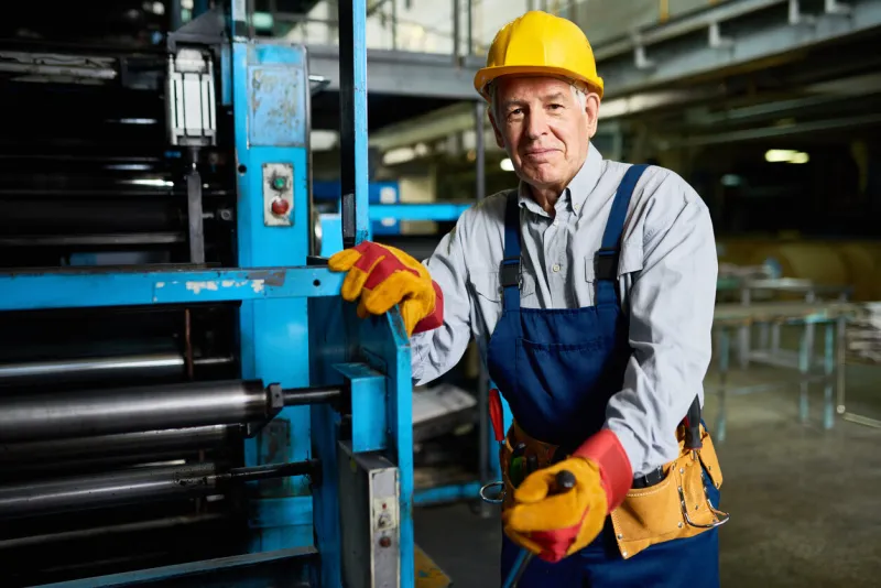 portrait of senior factory worker smiling looking at camera standing by machine in modern industrial workshop