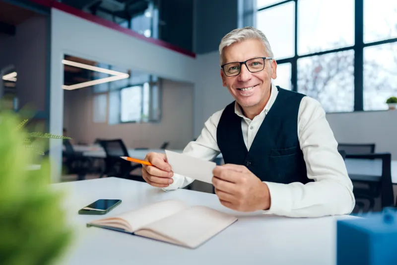 busy senior man sitting at office desk with papers and making notes close up