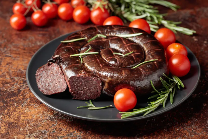 black pudding or blood sausage with rosemary and tomatoes on a black plate