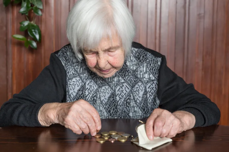 elderly 95 years old woman sitting miserably at the table at home and counting remaining coins from the pension in her wallet after paying the bills