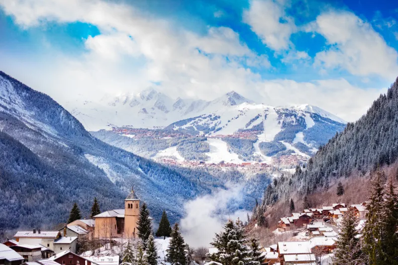 panorama of champagny-en-vanoise village with mist and clouds around old church, over courchevel resort on background