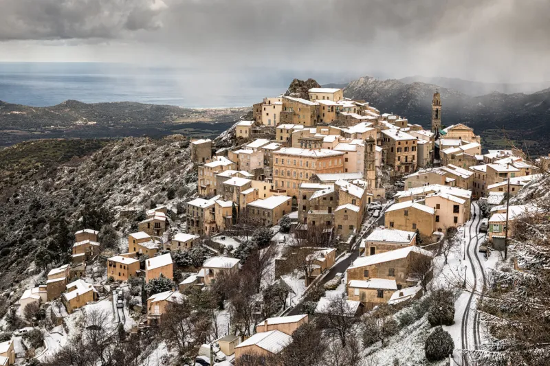 snow and dark clouds cover the ancient mountain village of speloncato in the balagne region of corsica
