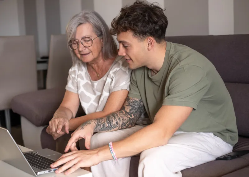 senior woman and young boy smiling looking together at laptop at home happy nephew teaching new computer technology to his old grandmother old woman learns to use computer