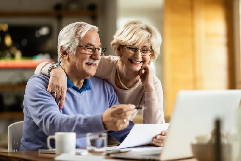 happy senior couple going through home finances and using computer at home