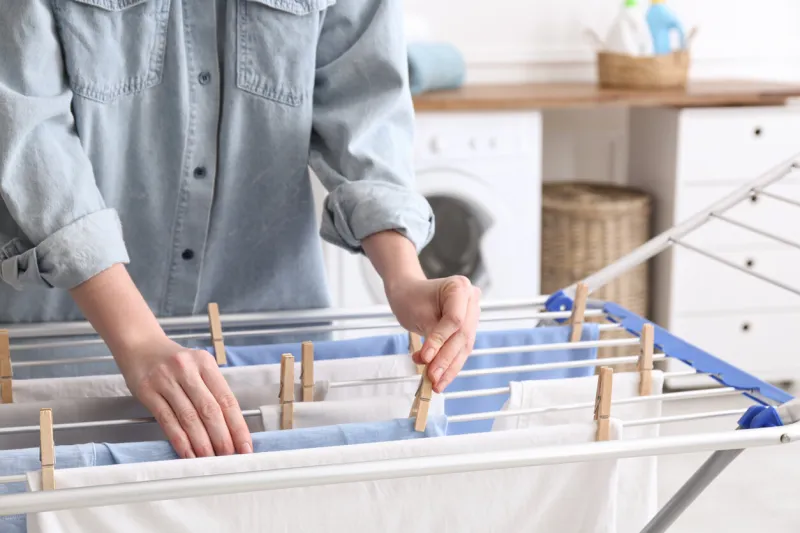 woman hanging clean laundry on drying rack in bathroom, closeup