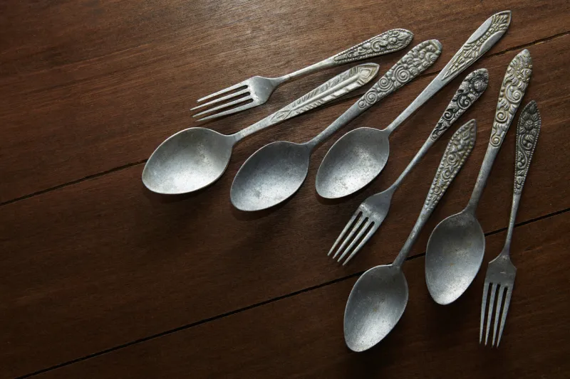 several old spoons and forks made of silver with antique ornaments on the handles on a wooden table