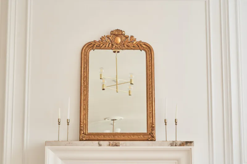 a mirror in a classic frame on the mantelpiece next to candlesticks with candles part of the interior with a reflection of the chandelier on the ceiling classic interior with copy space