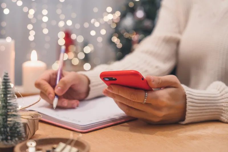 goals plans make to do and wish list for new year christmas concept writing in notebook woman hand holding pen on notepad and cellphone at home on winter holidays xmas