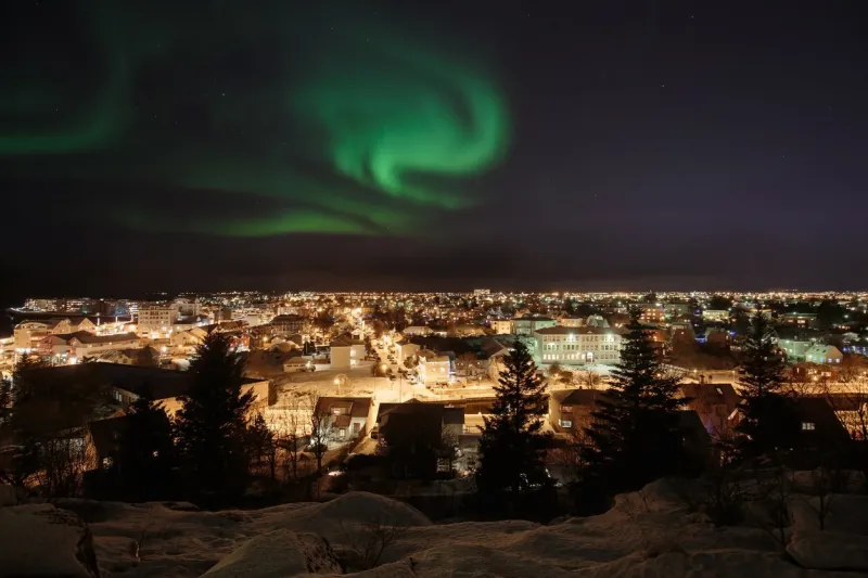 auroras blazing in the sky above the reykjavik area in iceland around christmas time, snow on the ground