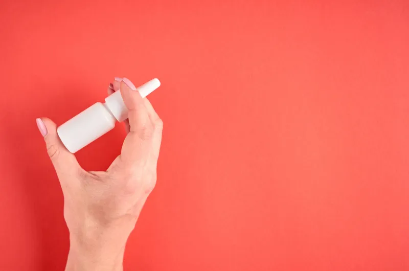 nasal spray bottle composition with hand, white template bottle on pink background, flat lay and top view photo