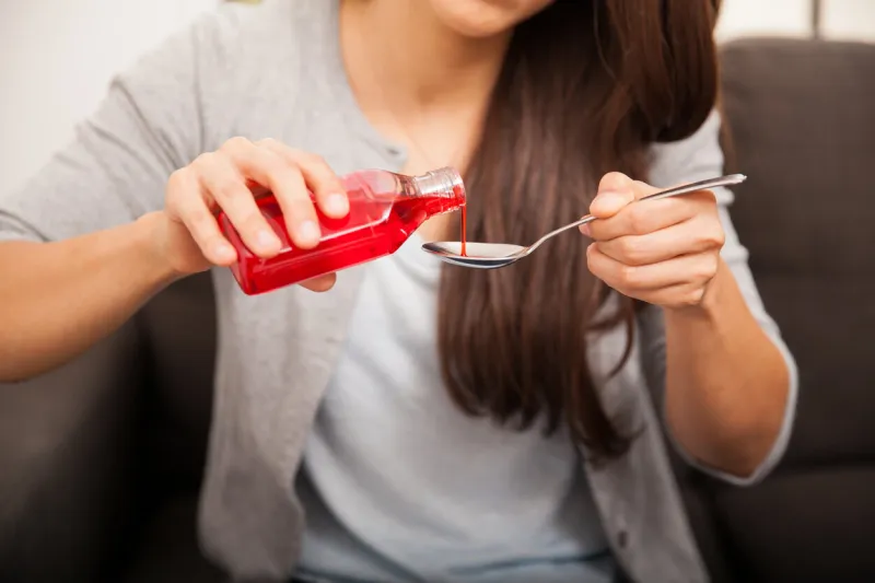 closeup of a young brunette pouring some cough syrup in a spoon at home