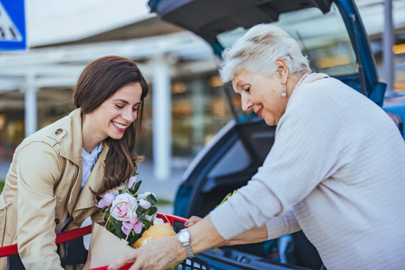 two women happily load groceries into their car trunk outside a supermarket the scene captures friendship, collaboration, and a sense of community