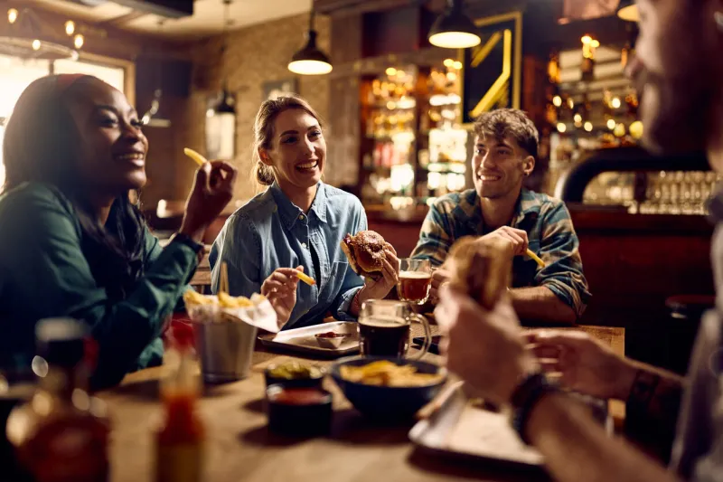 multiracial group of happy friends eating burgers while drinking beer in a pub