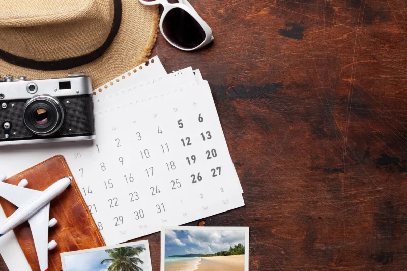 travel vacation background concept with calendar, sun hat, camera, passport, airplane toy and weekend photos on wooden backdrop top view with copy space flat lay all photos taken by me