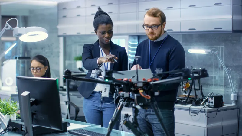 caucasian male and black female engineers working on a drone project with help of laptop and taking notes he works in a bright modern high-tech laboratory