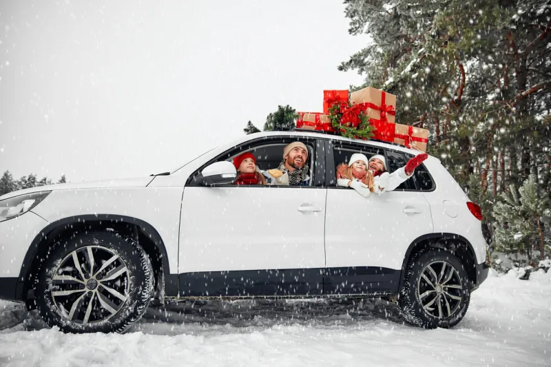merry christmas and happy new year happy family with children sitting in a car loaded with boxes of gifts and a christmas tree against the background of a forest in snowy weather