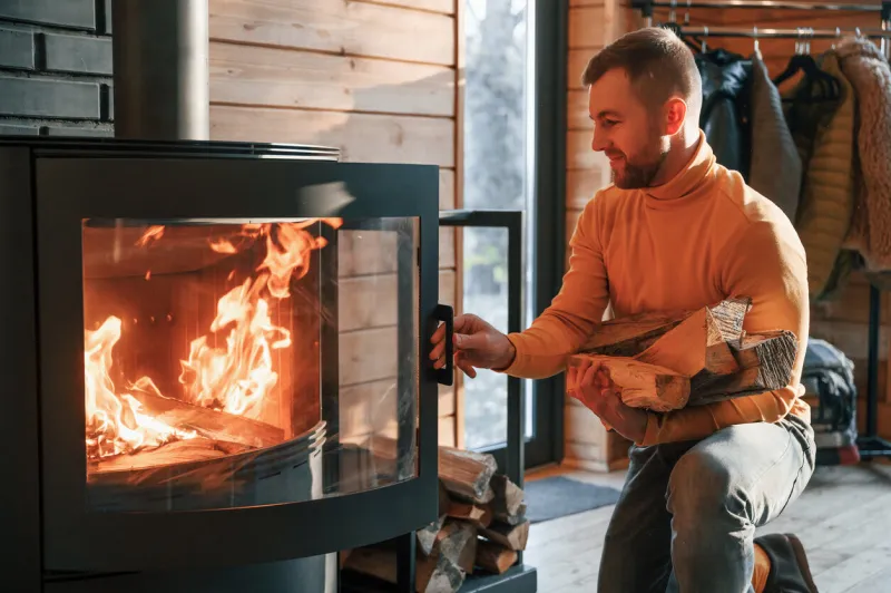 man is putting wood into the fireplace indoors in the house