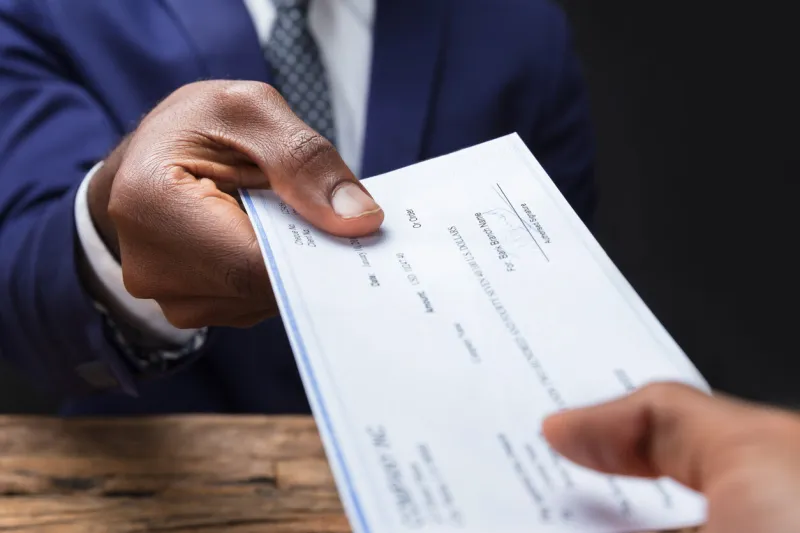 close-up of a businessman's hand giving cheque to colleague over wooden desk