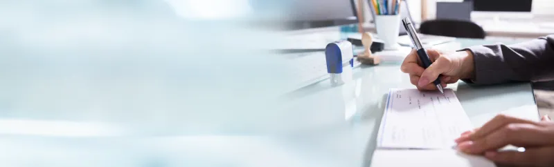 close-up of a businessman filling the cheque with pen on reflective desk in office