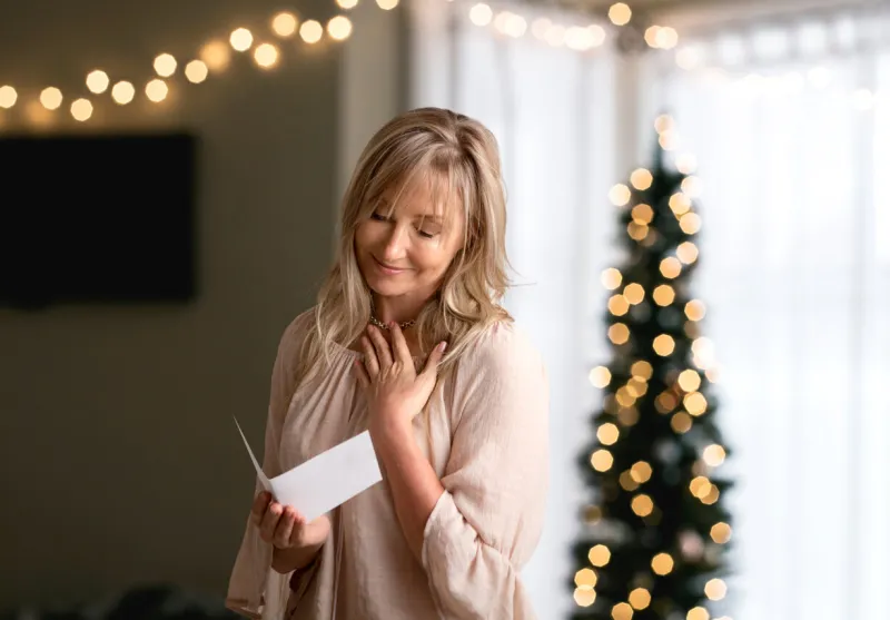woman reading a heartfelt message in a card at christmas time she is smiling and has her hand to heart