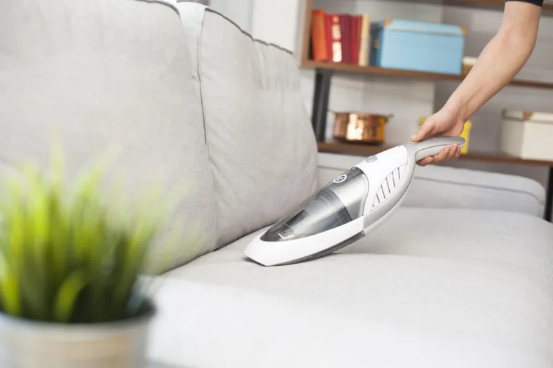 woman with handheld vacuum cleaning on sofa