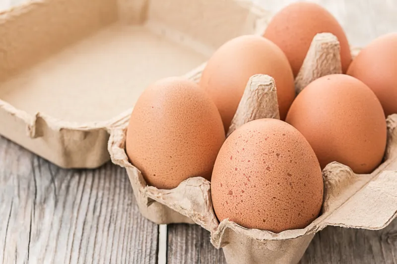 fresh brown eggs in carton on wooden table