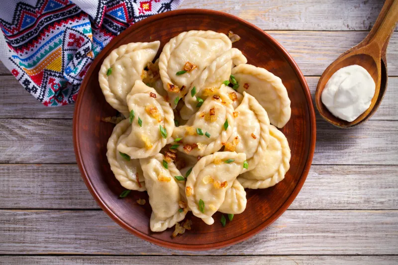 dumplings, filled with potato dumplings with filling and sour cream in wooden spoon overhead, horizontal