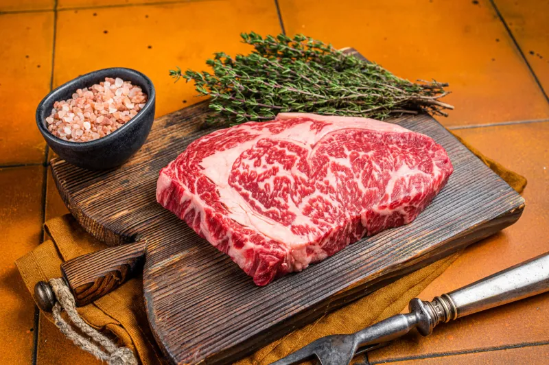 prime raw wagyu rib eye beef meat steak on wooden board orange background top view