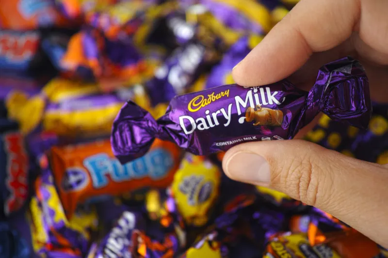 paphos, cyprus - november 27, 2015  cadbury dairy milk candy in womans hand with background of cadbury candies