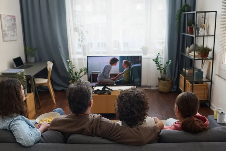rear view of family of four sitting together on sofa and enjoying watching the movie