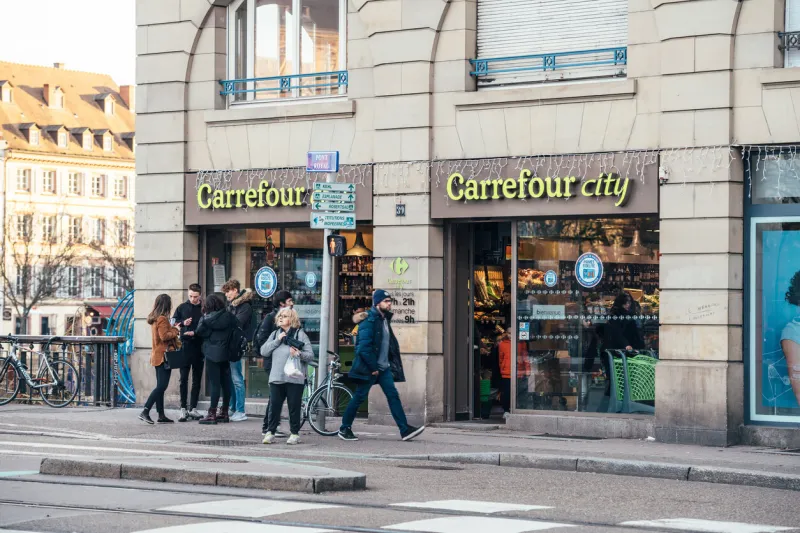 strasbourg, france - feb 14, 2019  crowd of people in front of carrefour city food supermarket store with large glass entrance doors