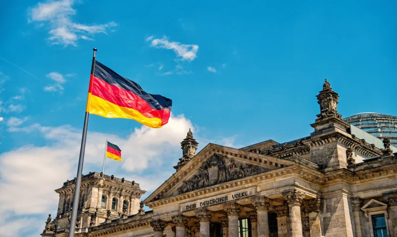 german flags waving in the wind at famous reichstag building, seat of the german parliament deutscher bundestag , on a sunny day with blue sky and clouds, central berlin mitte district, germany