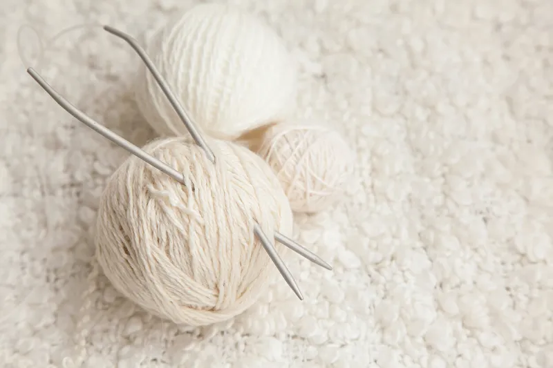 set of three white balls and knitting needles on a white knitted blanket
