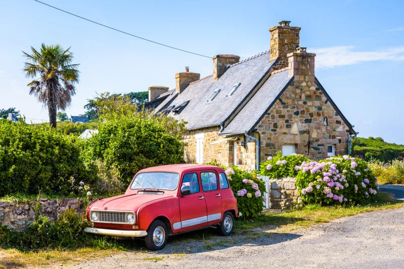 plougrescant, france - august 3, 2019  a renault 4 classic french car is parked in front of a typical granite house in brittany with slate roof, palm tree and hydrangea by a sunny summer day
