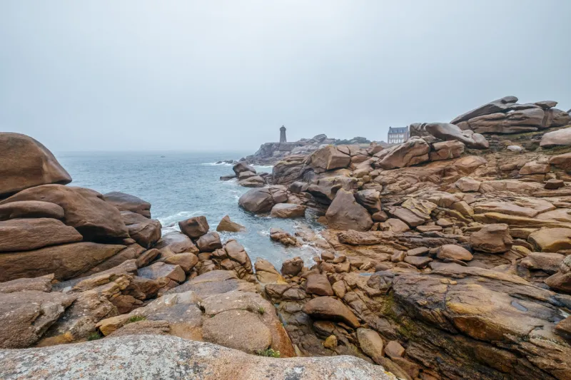 pink granite coast at ploumanac'h with the lighthouse in a foggy day in brittany, france