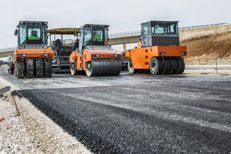 pavement machine laying fresh asphalt or bitumen on top of the gravel base during highway construction