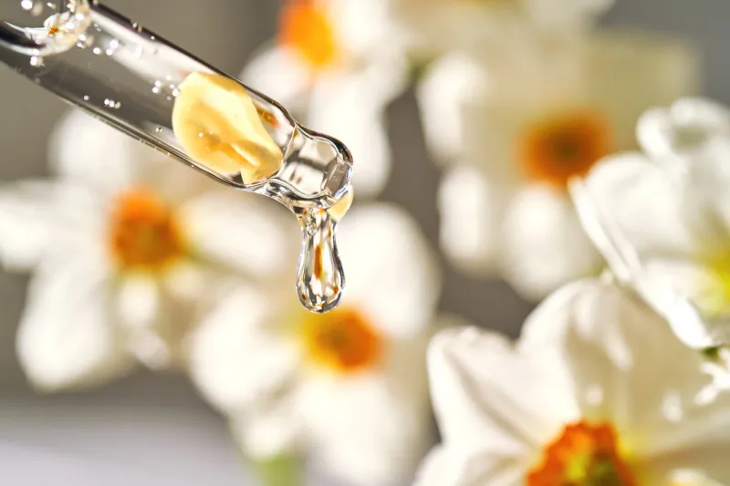 an eyedropper with a cosmetic product on the background of daffodils