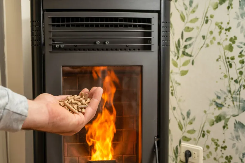 man's hand holding pellets in front of the glass of a stove with a beautiful flame, sustainable and ecological heating