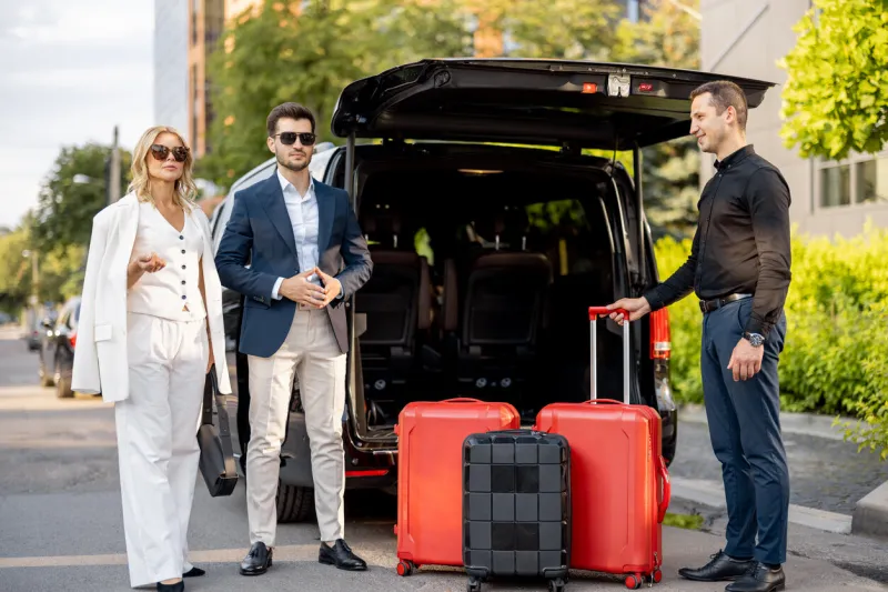 business couple standing by a minivan taxi waiting for their chauffeur or porter to help them with a suitcases concept of business trips and travel