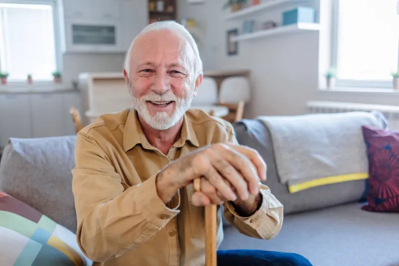 shot of an elderly man sitting on the couch with a walking stick at home senior man leaning in his walking stick at home