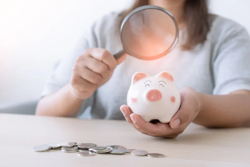 woman using magnifying glass to examine piggy bank concept of financial and money saving forecast future financial trend in the market tax, interest, or mortgage loan prediction from bank