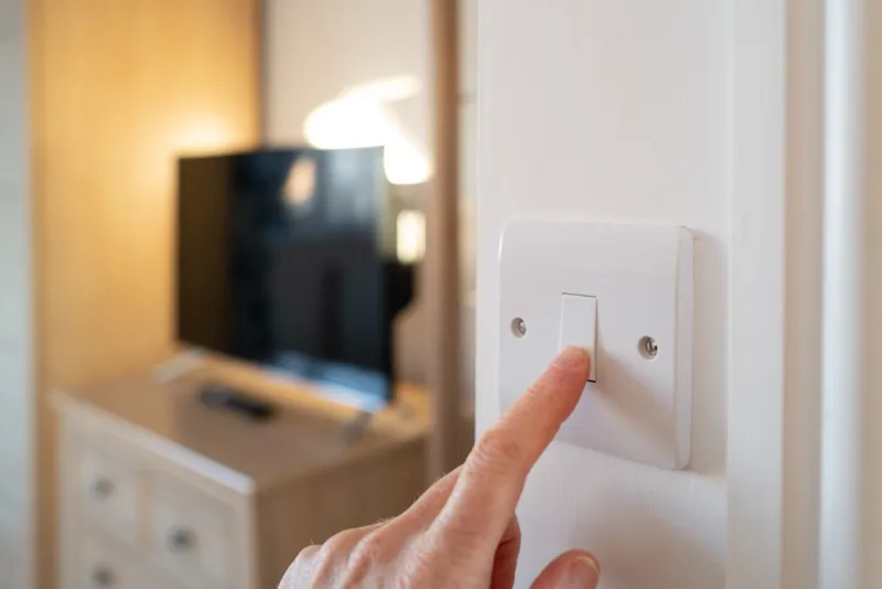 shallow focus of a home owner switching off a bedroom light after waking up in late morning a smart tv can be seen in the room