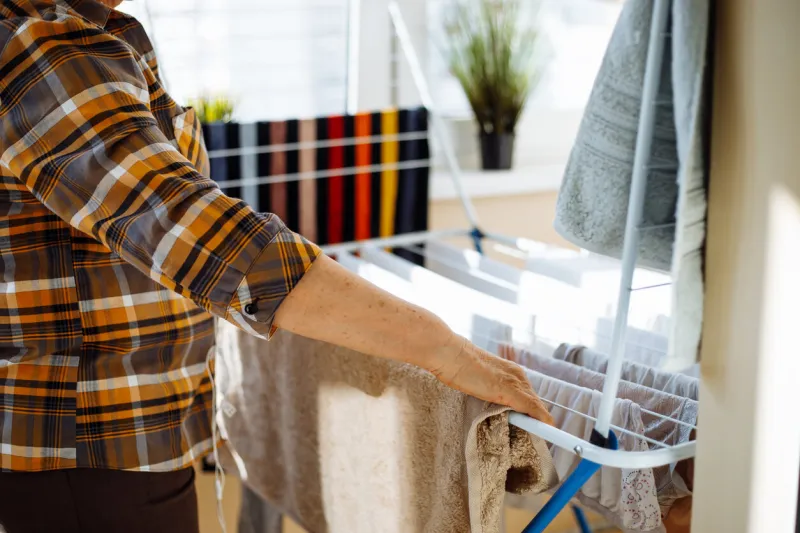 woman on sunny day standing in home room near clothesline board and hanging clean wet clothing back view closeup housewife tidy up house and arranging fresh clothes house cleaning concept