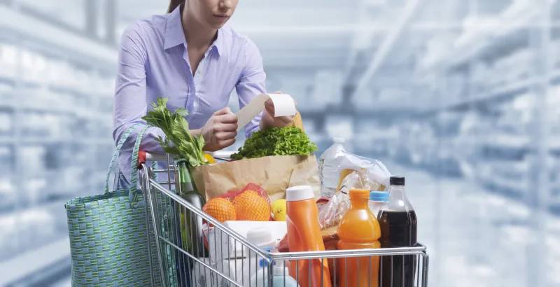 woman pushing a cart and checking a grocery receipt, grocery shopping and expenses concept