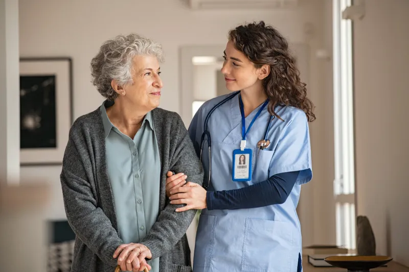 young caregiver helping senior woman walking nurse assisting her old woman patient at nursing home senior woman with walking stick being helped by nurse at home