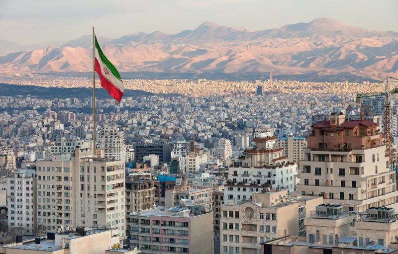 aerial view of tehran skyline at sunset with large iran flag waving in the wind