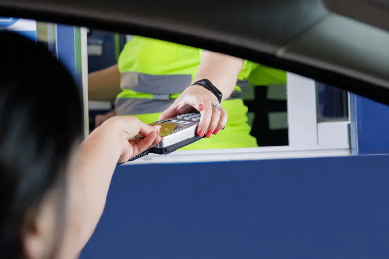 unrecognizable woman paying with a bank card at a pos of an operator, also unrecognizable, of a toll road