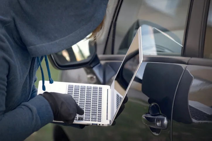hooded thief tries to break the car's security systems with laptop hacking modern car concept