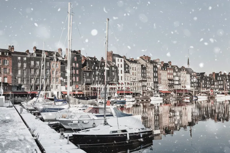honfleur harbour quay in normandy, france in winter snowstorm magic famous snowy cityscape with houses reflection in the water christmas mood background monochromatic neutral tones, natural light