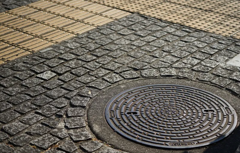 cobblestones and manhole covers on the ground on the sidewalk of city street on a sunny day